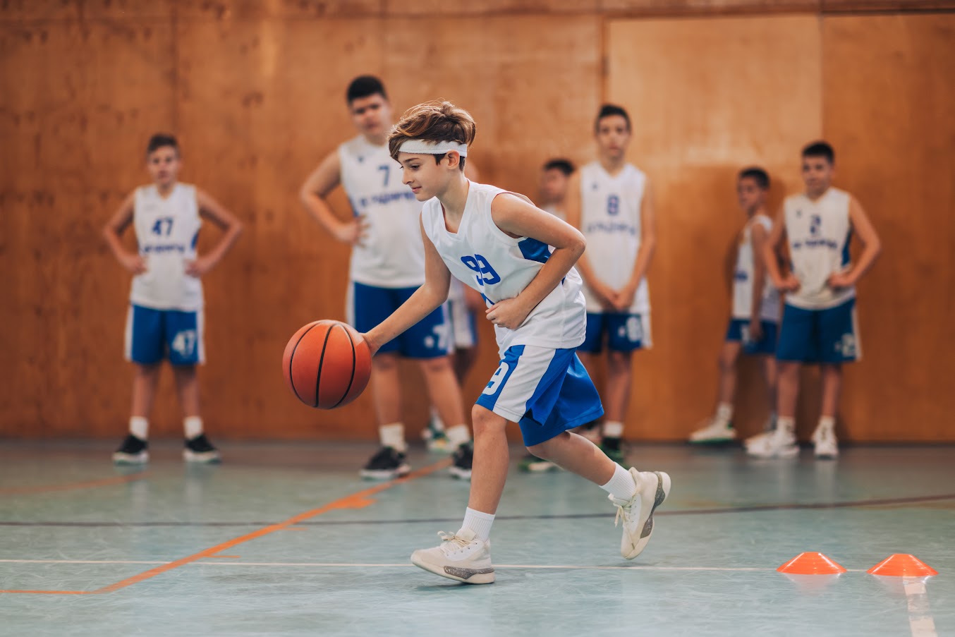 Junge beim Basketballtraining dribbelt den Ball in einer Sporthalle während andere Kinder im Team zuschauen